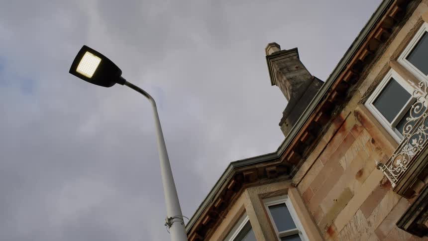 A low-angle shot of a bright LED street lamp against an overcast sky next to a traditional stone building