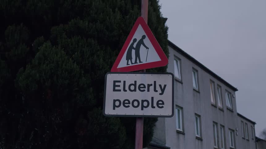 A static shot of a road sign warning of elderly people crossing with a residential building in the background