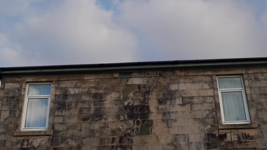 Static shot of two white-framed windows on an old weathered stone building with a cloudy sky above