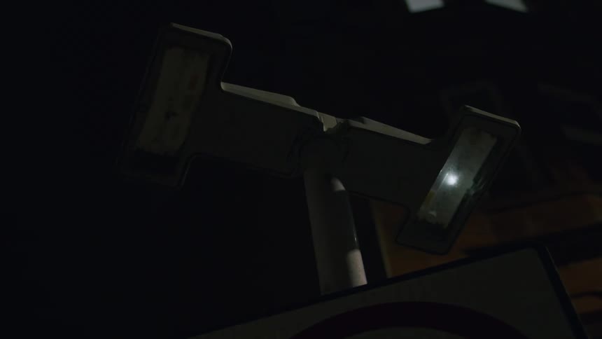 A low-angle close-up of a traffic sign light flashing repeatedly on a dark city street at night