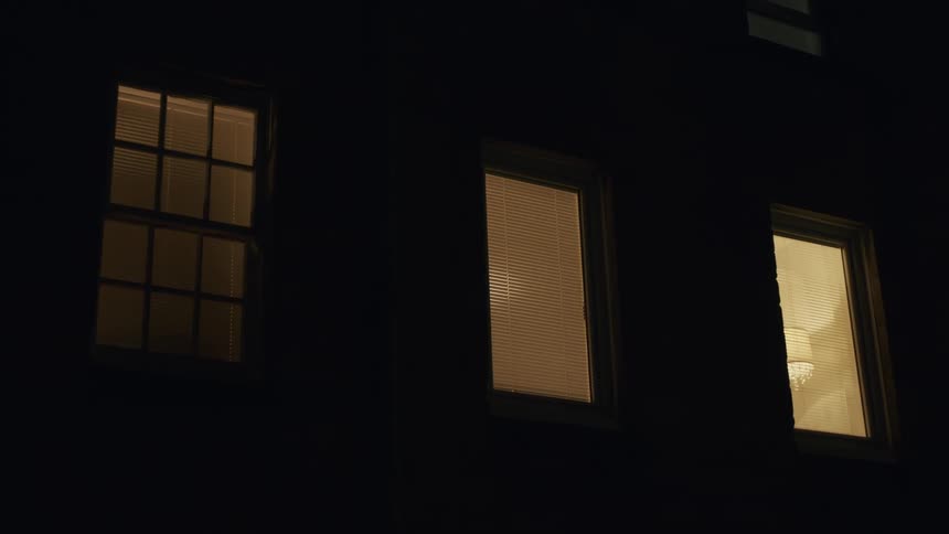 Three illuminated windows with blinds show a warm glow