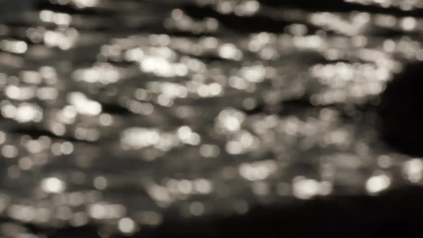 An out-of-focus shot of sparkling bokeh lights reflecting and shimmering on the dark surface of moving water