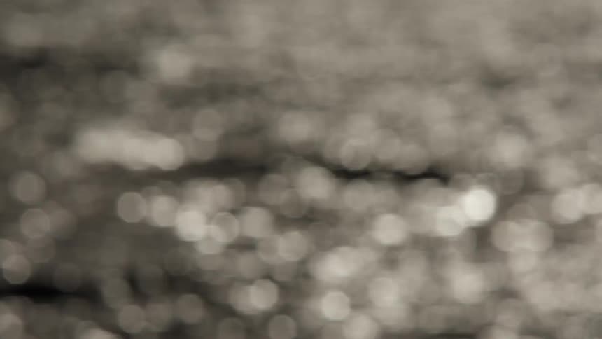 Calm and abstract bokeh footage of sunlight reflecting on gently rippling water in a sepia tone