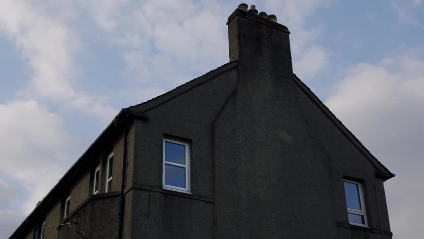 Low angle view of a weathered building with a chimney as clouds float by in the sky