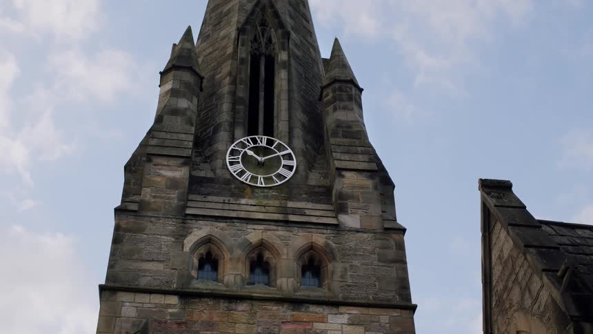 Low angle shot of a historic stone church clock tower against a cloudy blue sky