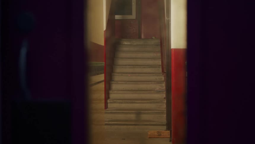 A mysterious shot of a dimly lit, dusty staircase inside an old building as seen through a doorway