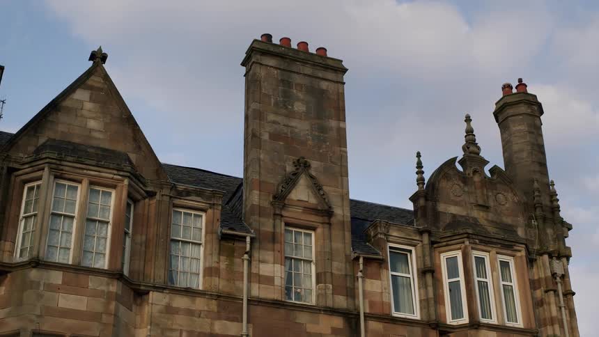 Low angle static view of an old stone manor with ornate architecture and chimneys against a partly cloudy sky