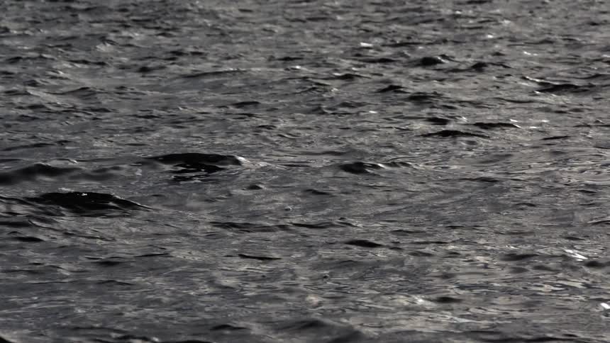 A slow-motion close-up of a dark, rippling body of water flowing peacefully