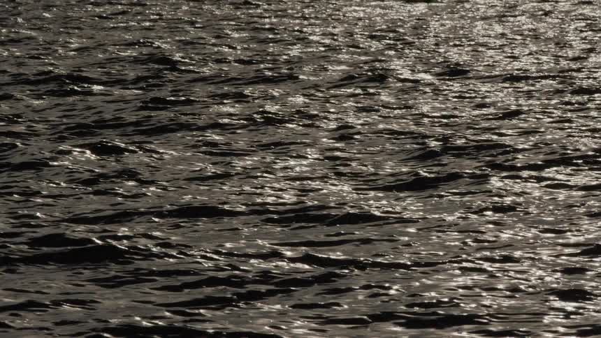 Slow motion shot of a dark water surface with shimmering light reflections