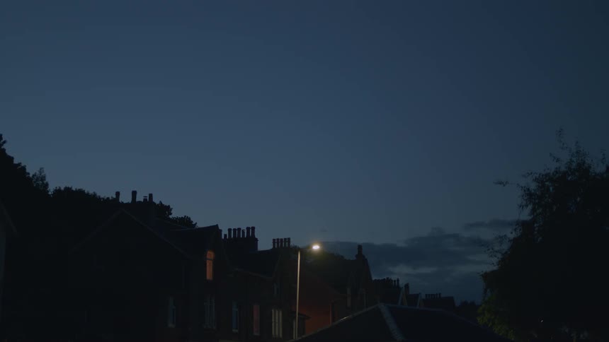 A street light over a row of silhouetted houses against a deep blue sky at dusk
