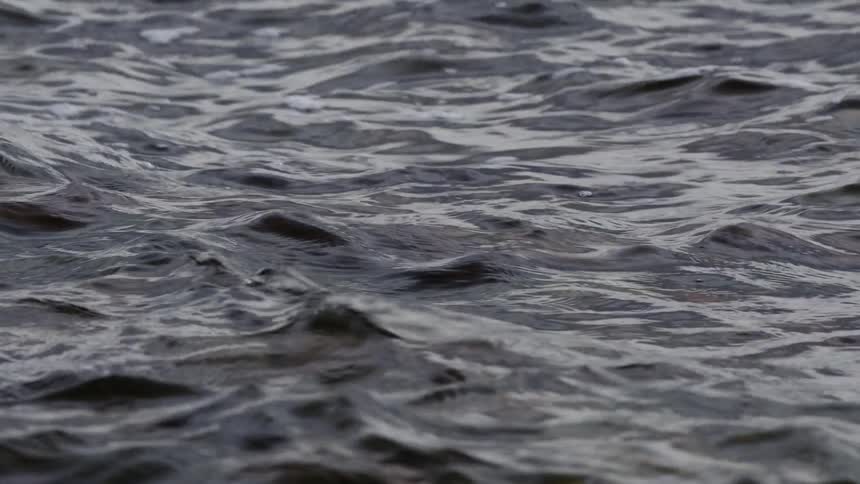 A mesmerizing slow-motion close-up of dark, moody water with gentle waves and ripples
