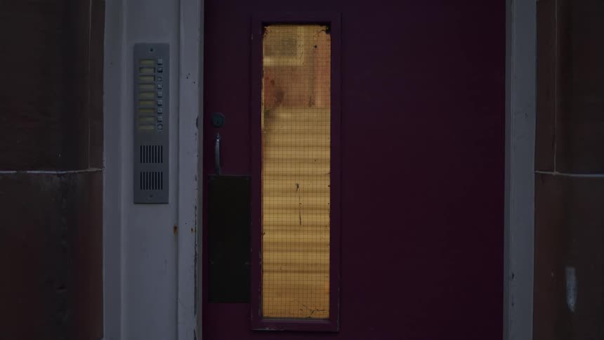 Interior stairs of a building, seen through the reinforced glass window of a door at night