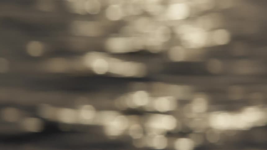 Calm, abstract background of sepia-toned sunlight sparkling with a bokeh effect on the surface of gently rippling water