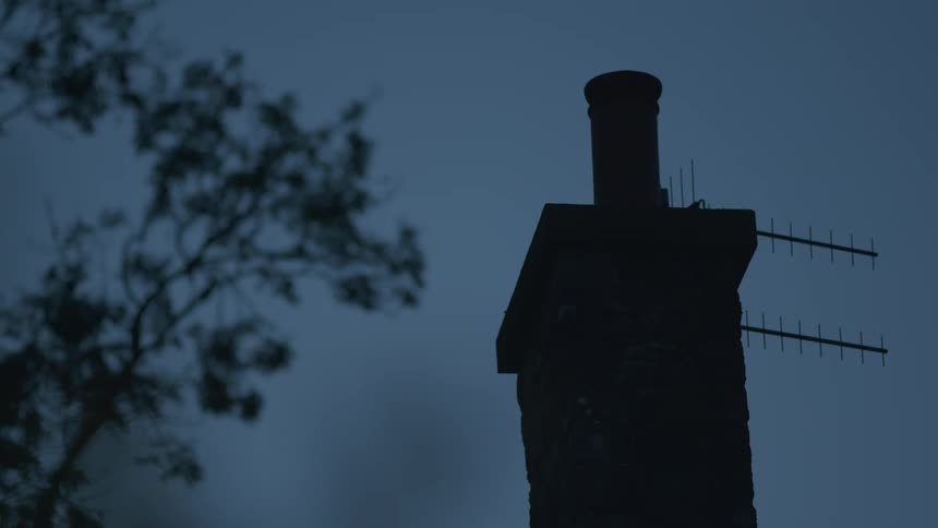 A silhouetted brick chimney against a gloomy twilight sky