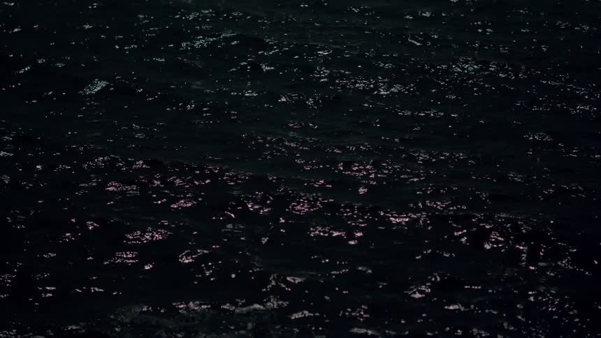 Dark ocean water gently ripples at night with sparkling light reflecting on the surface