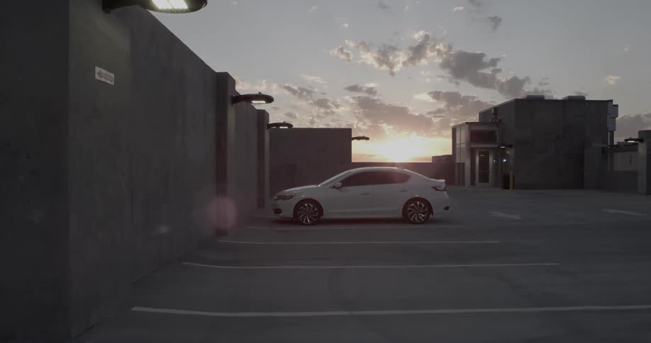A white car sits parked in an empty parking lot at dawn