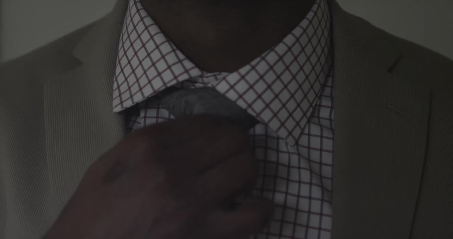 A dark skinned man wearing a suite adjusts his necktie