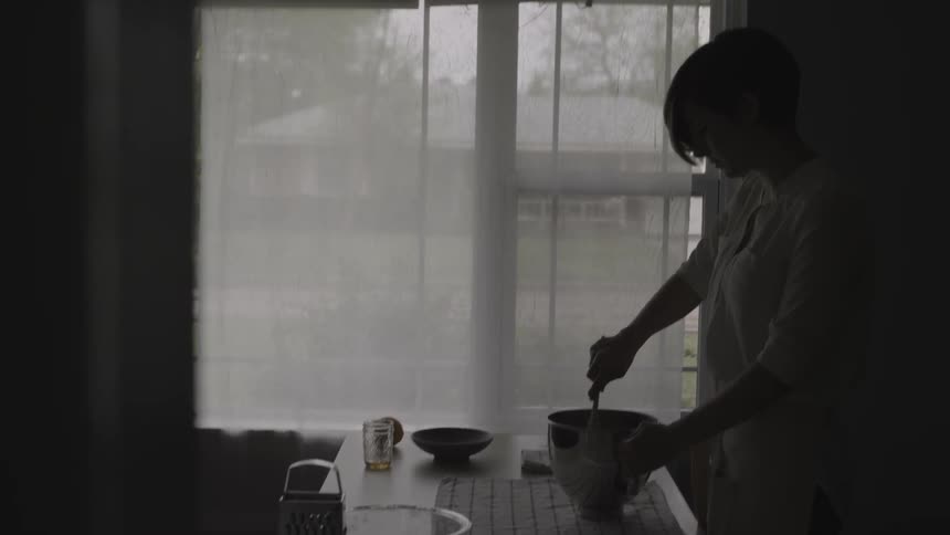 A woman is mixing something in the dark kitchen