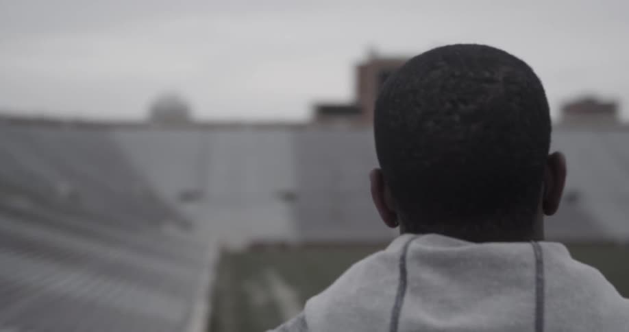 A man stands before a sports field on a cloudy day