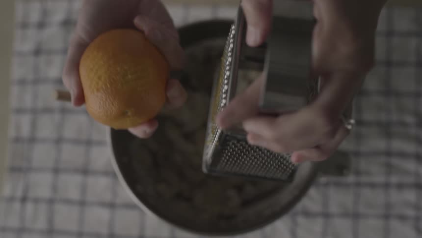 A woman zest orange over a mixing bowl