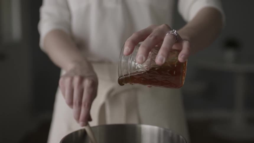 A woman pours honey into a cooking pot