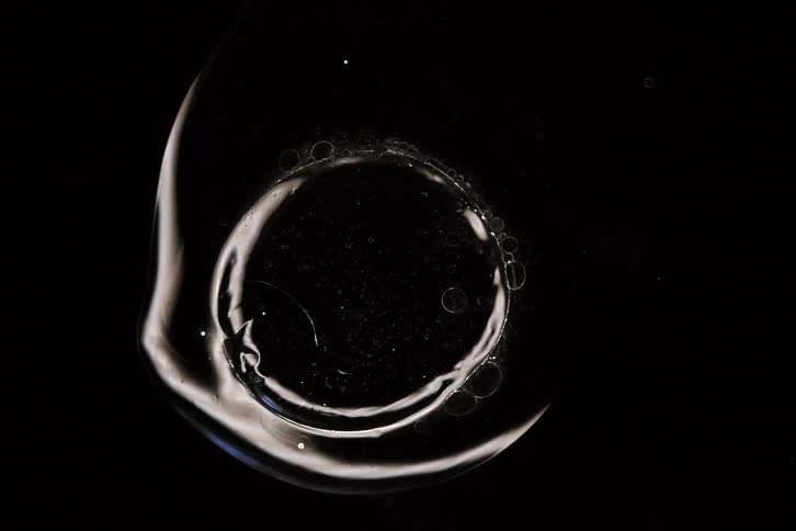 A mesmerizing macro shot of a clear, viscous liquid with shifting air bubbles against a stark black background