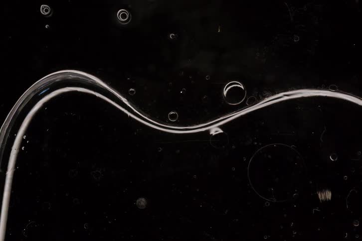 A clear, viscous liquid slowly forms a sinuous wave in this abstract macro shot against a black background
