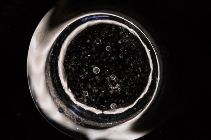 Mesmerizing macro shot of a static, circular chemical reaction with suspended particles against a stark black background
