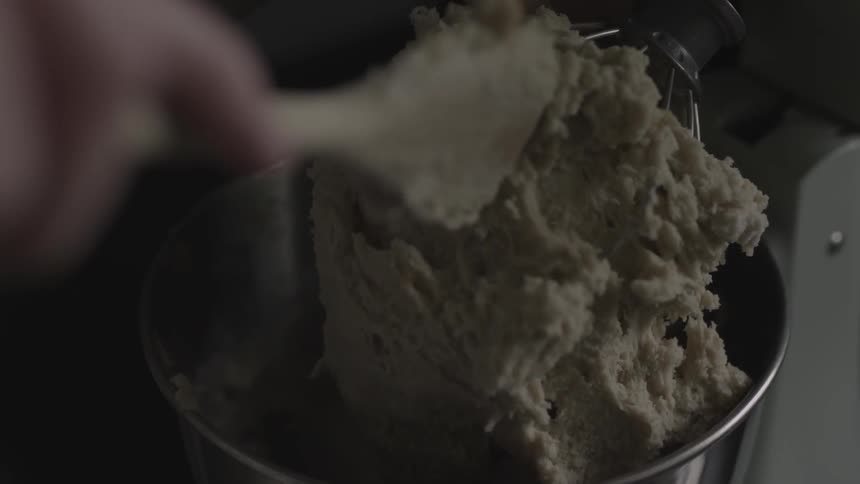 A person lifts a mixer and spoons batter off the whisks