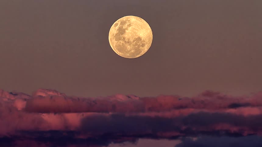 A stunning time-lapse captures a golden full moon rising through beautiful pink and purple clouds at dusk