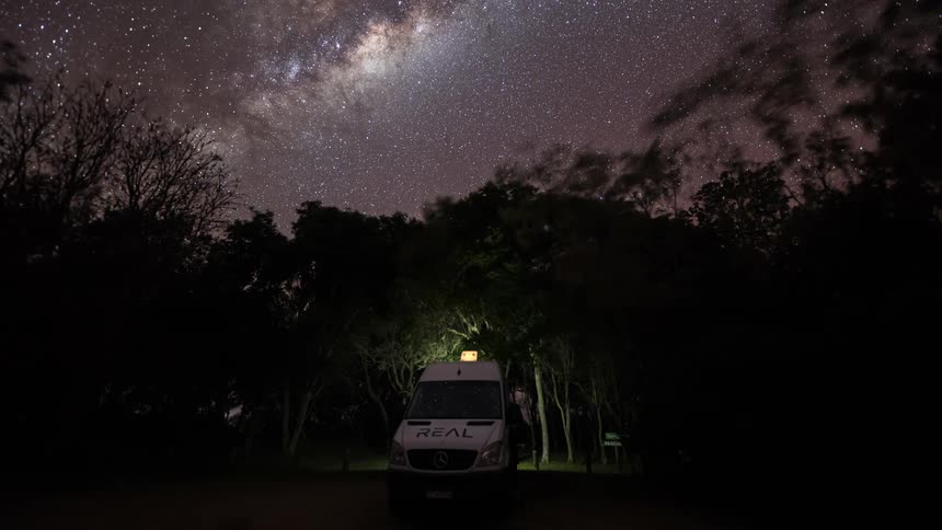 A stunning timelapse of the Milky Way galaxy moving across the starry night sky above a camper van parked in a dark, wooded area