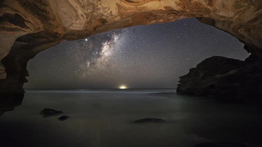 A stunning time-lapse from inside a seaside cave captures the Milky Way galaxy rotating across the night sky over the calm ocean