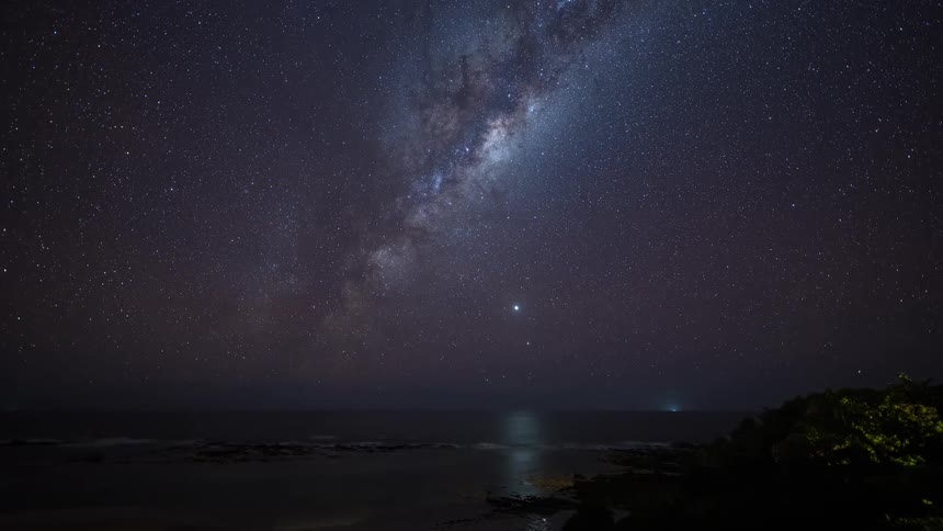 A breathtaking timelapse captures the Milky Way galaxy rotating through the starry night sky above a tranquil ocean coast
