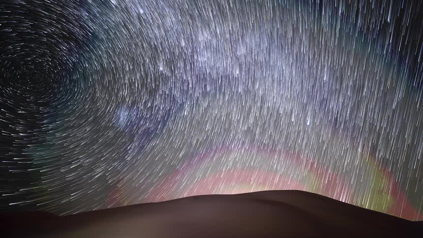 A mesmerizing timelapse captures stars creating swirling trails and a vortex over a desert landscape