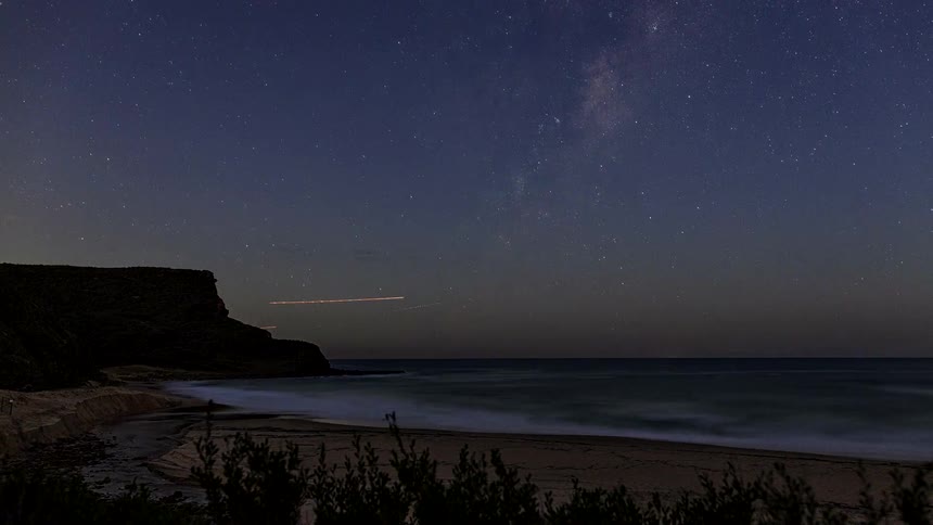 An epic day-to-night timelapse captures a vibrant sunset over a secluded beach, transitioning into a spectacular view of the Milky Way galaxy