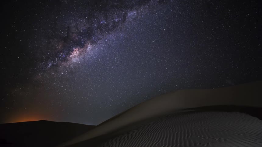 A breathtaking time-lapse shows the Milky Way galaxy moving across a star-filled night sky over vast desert sand dunes until dawn