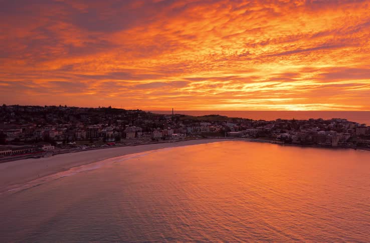 An incredible aerial view shows a fiery red sunrise over the iconic Bondi Beach in Sydney, Australia, as the camera slowly reveals the coastline