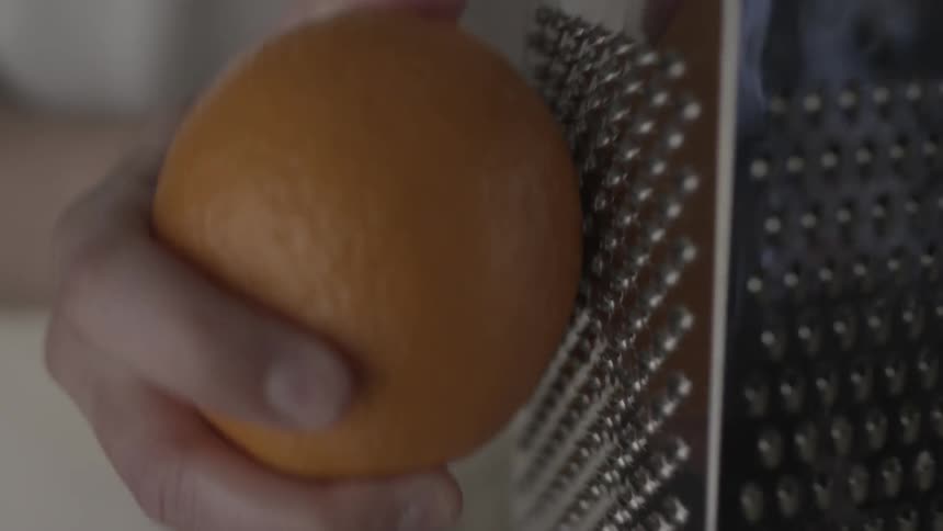 A person is shaving an orange on a shredder