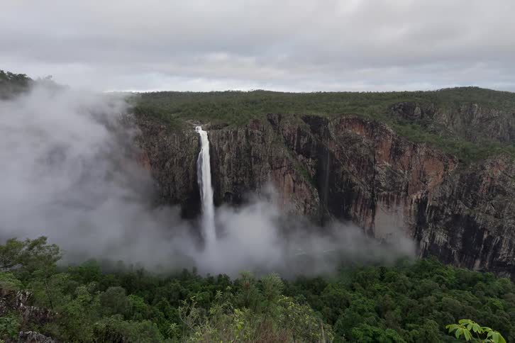 A stunning view of a waterfall cascading down a sheer cliff as mist rolls through the lush valley below
