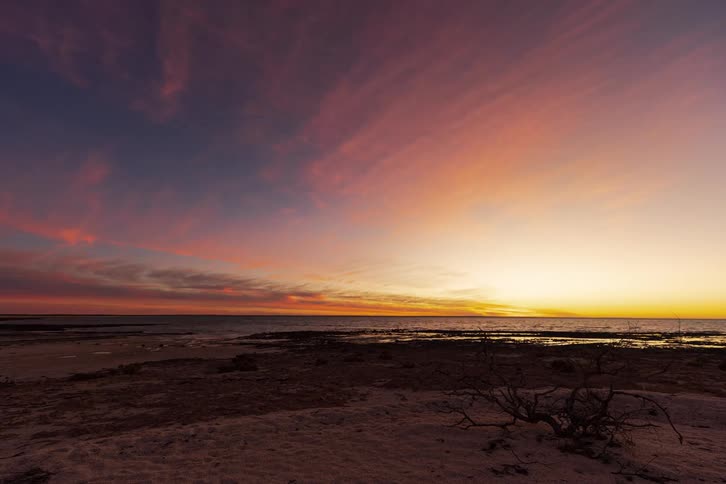 A beautiful day-to-night timelapse of a vibrant sunset over the ocean from a tranquil, sandy shoreline