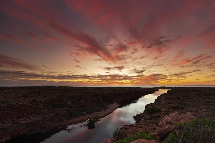 A stunning time-lapse of a vibrant, fiery sunset over a river flowing through a rocky landscape to the ocean