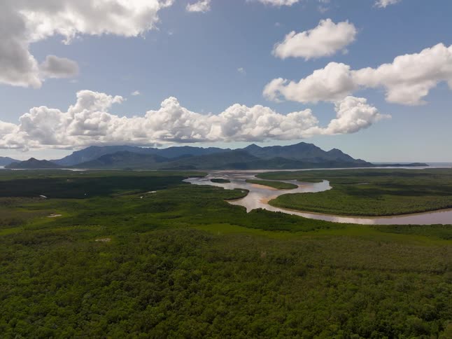 A timelapse aerial pullback shot reveals a vast tropical rainforest landscape with a winding river delta and distant mountains as clouds move across the sky