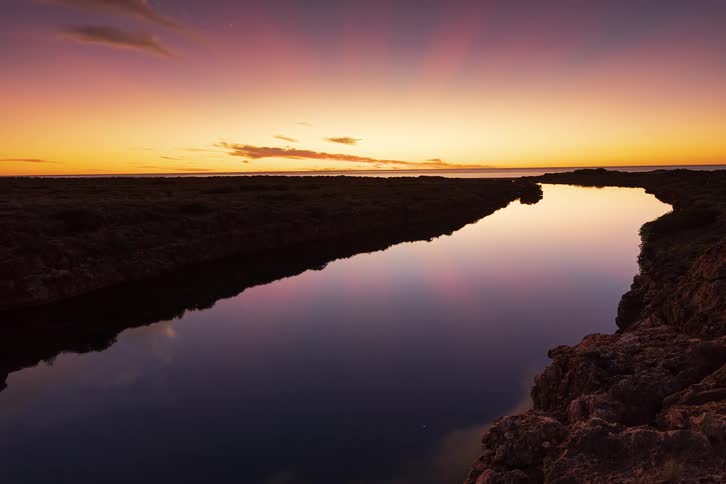 A stunning timelapse captures the vibrant colors of a sunset reflecting in a calm river leading to the ocean