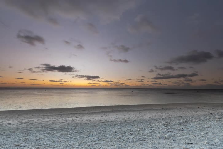 A breathtaking day-to-night timelapse captures a vibrant sunset over the calm ocean from a sandy beach