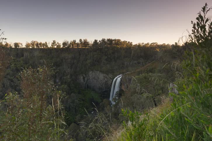 A beautiful time-lapse captures the sun rising over a majestic waterfall nestled in a deep, forested canyon