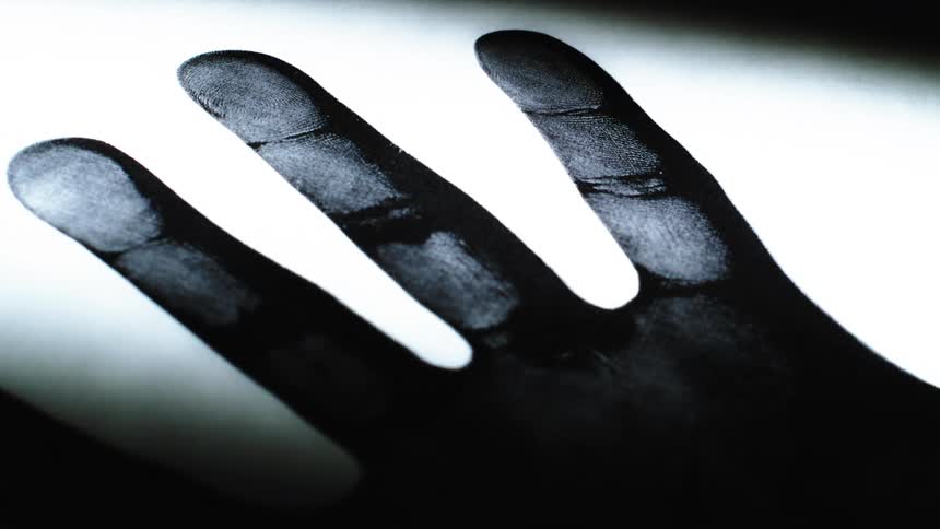 A stark black and white photocopy of a human hand is revealed by a moving light