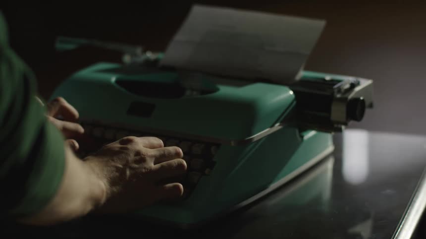 A close-up of a writer's hands typing on a vintage teal typewriter in a dramatically lit, dark room