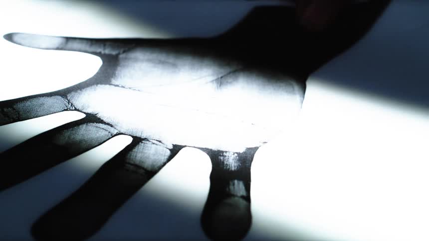 A mysterious handprint on a dark surface is slowly revealed and concealed by a sheet of paper under dramatic lighting