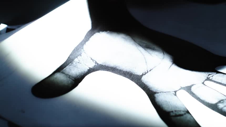 A mysterious light beam reveals a stark black and white handprint on paper before a real hand traces its lines