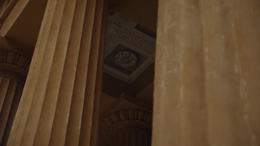 A low-angle view peeks through the stately, fluted columns of a historic building to reveal its ornate ceiling